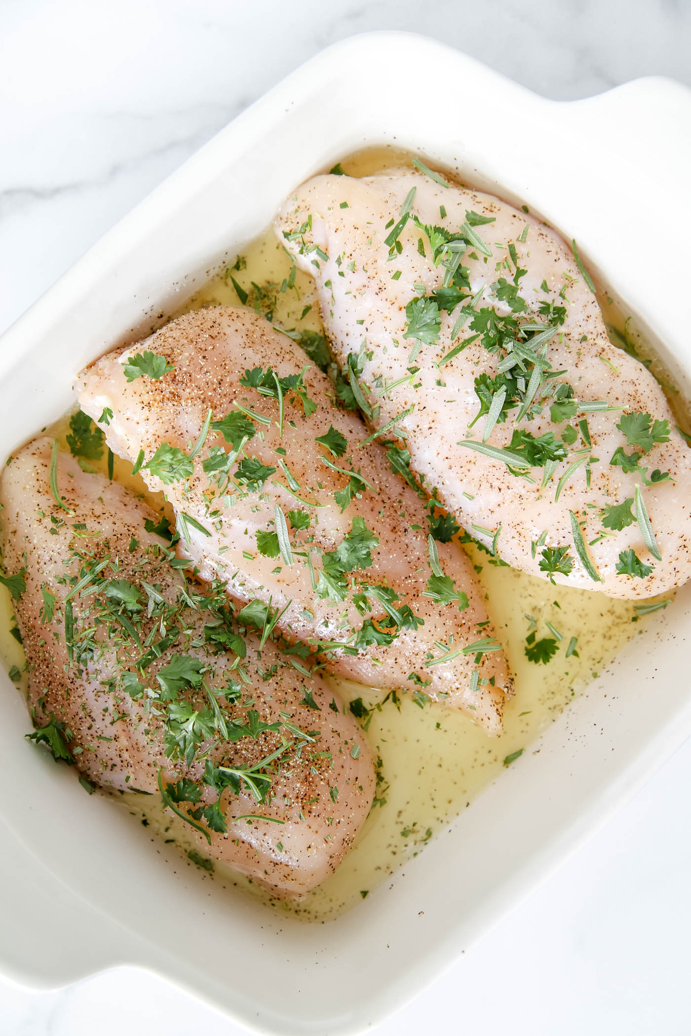 uncooked chicken breast with rosemary and parsley