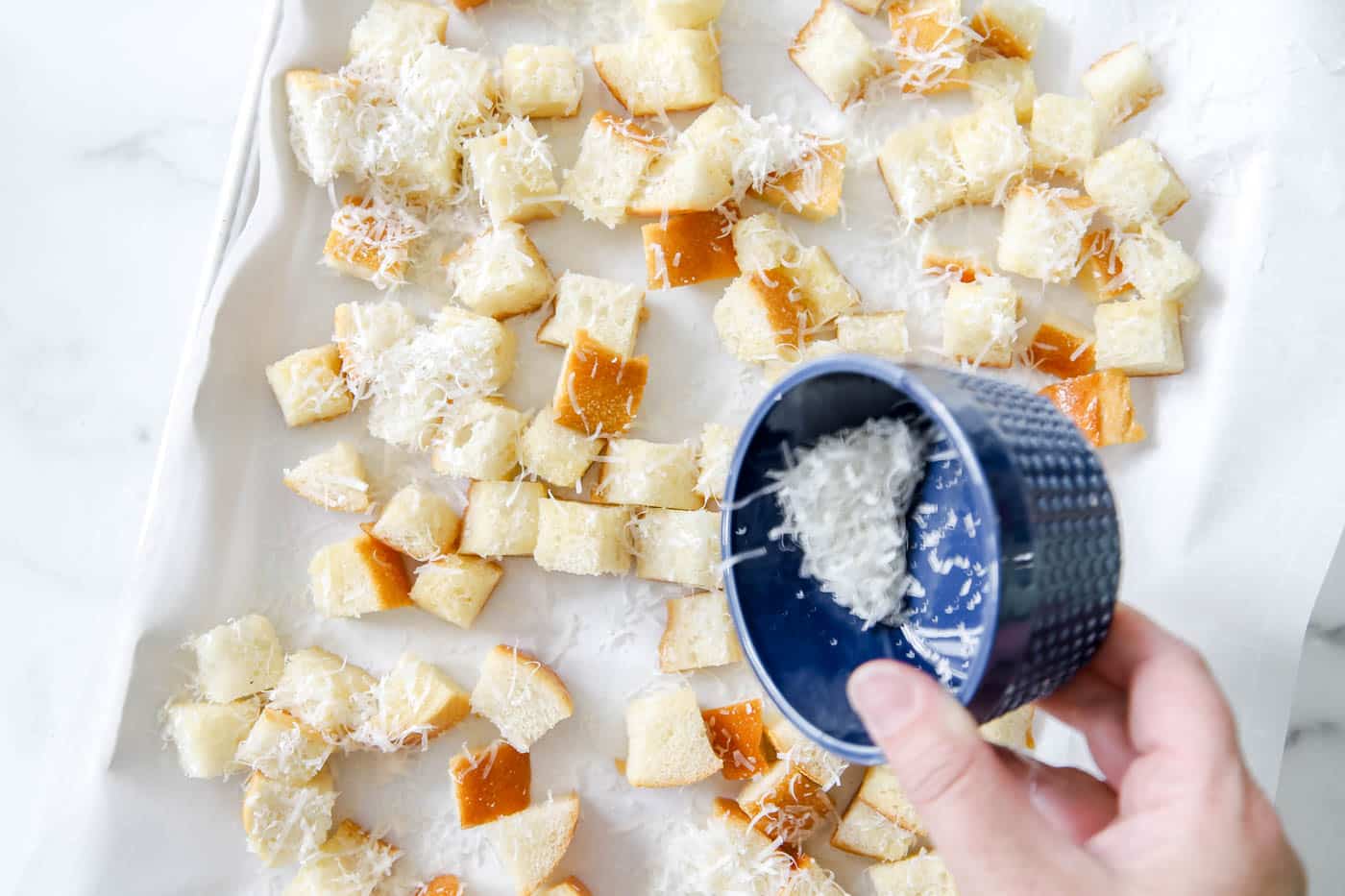 Place the croutons in a single layer on a parchment-lined baking sheet and sprinkle with 1/3 cup grated parmesan cheese.