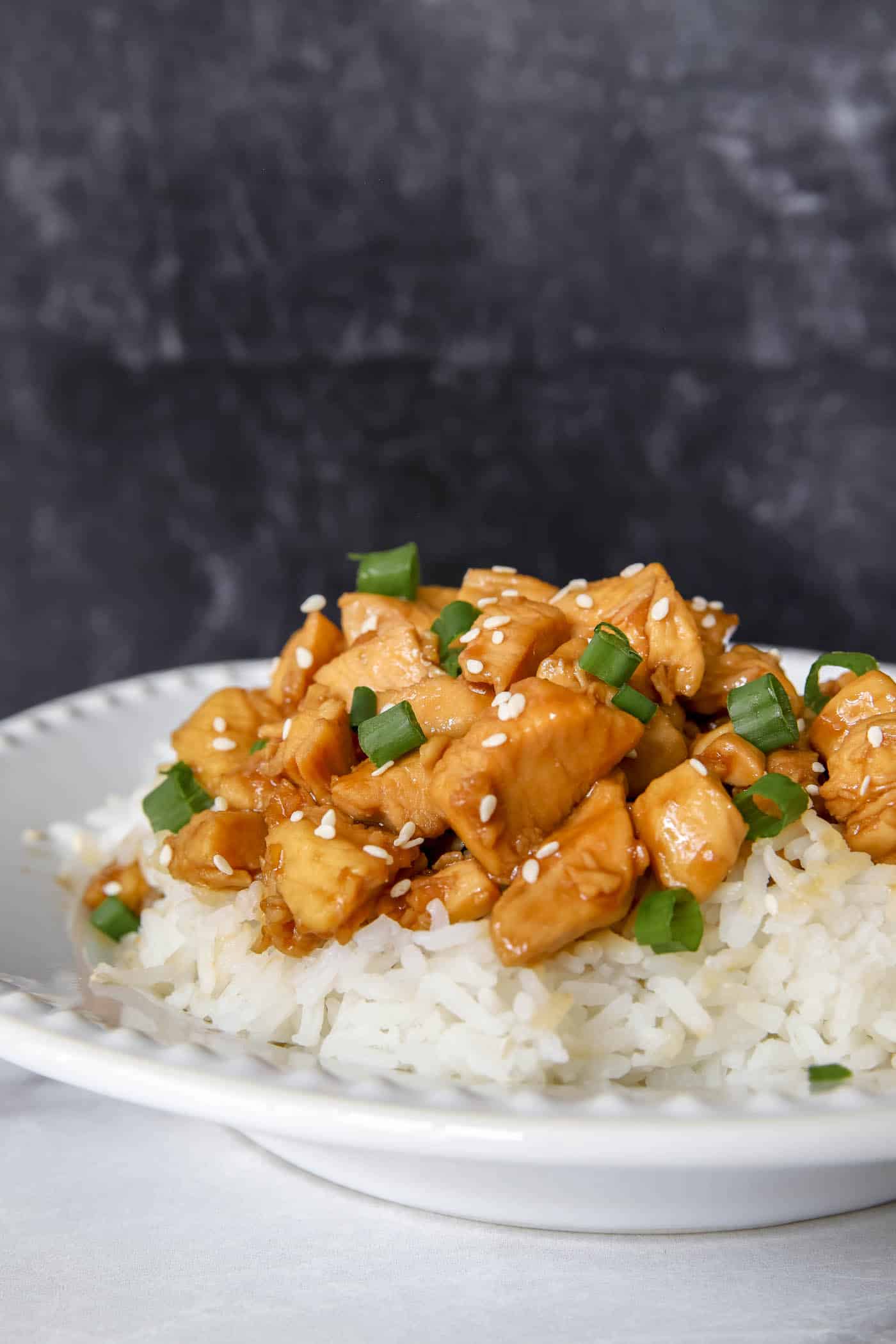 teriyaki chicken on rice and a white place with a black background.