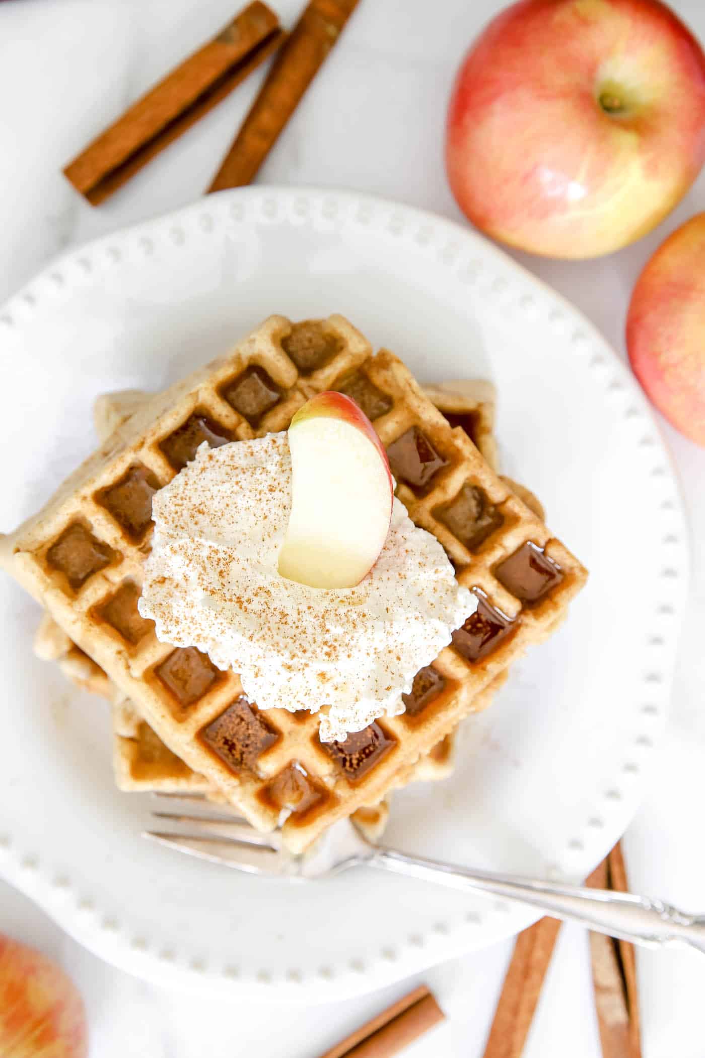 apple cinnamon waffles with whipped cream on top on a white plate.