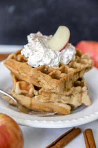 apple cinnamon waffles topped with homemade whipped cream and apple slice.