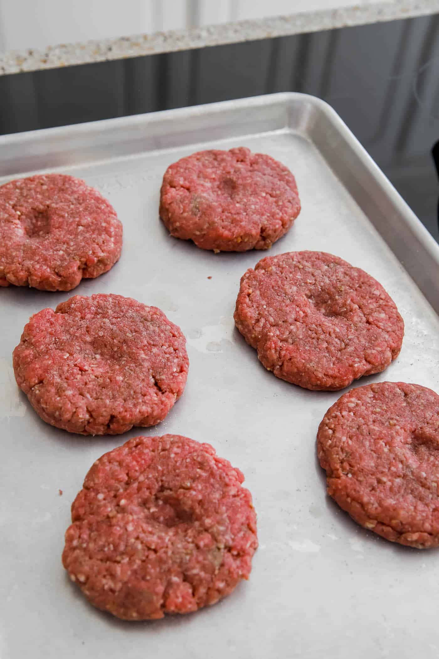 raw burgers in a sheet pan for cooking in the oven.