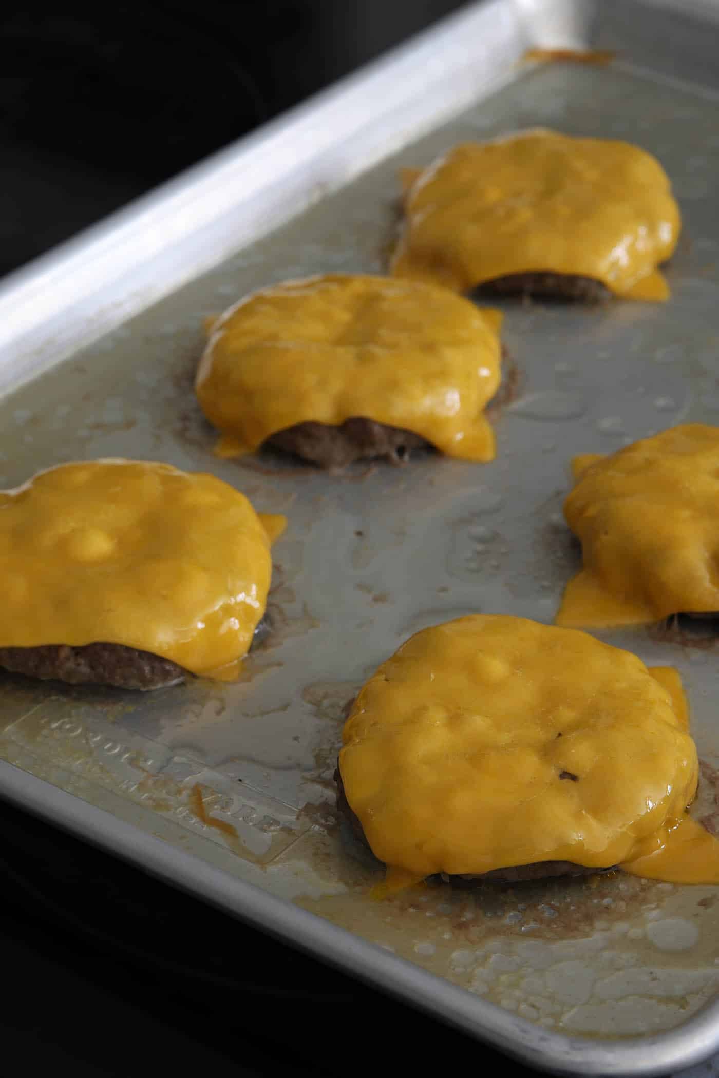 burger on a pan with melted cheese on top.