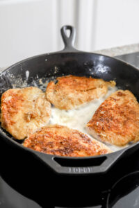 chicken cooking in cast iron skillet for parmesan chicken