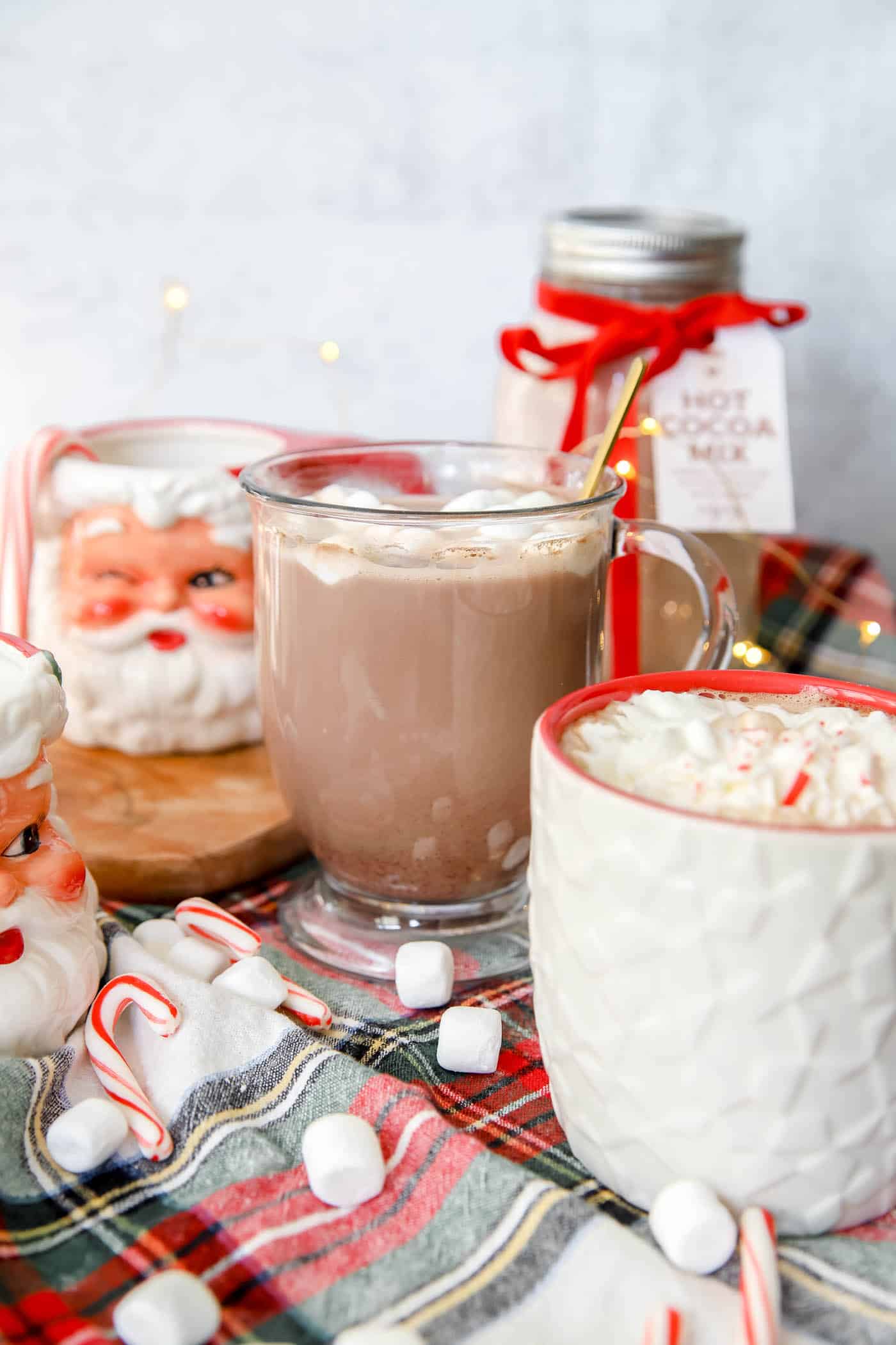 Hot chocolate in a mug with Santa mug and plaid table runner for Christmas.