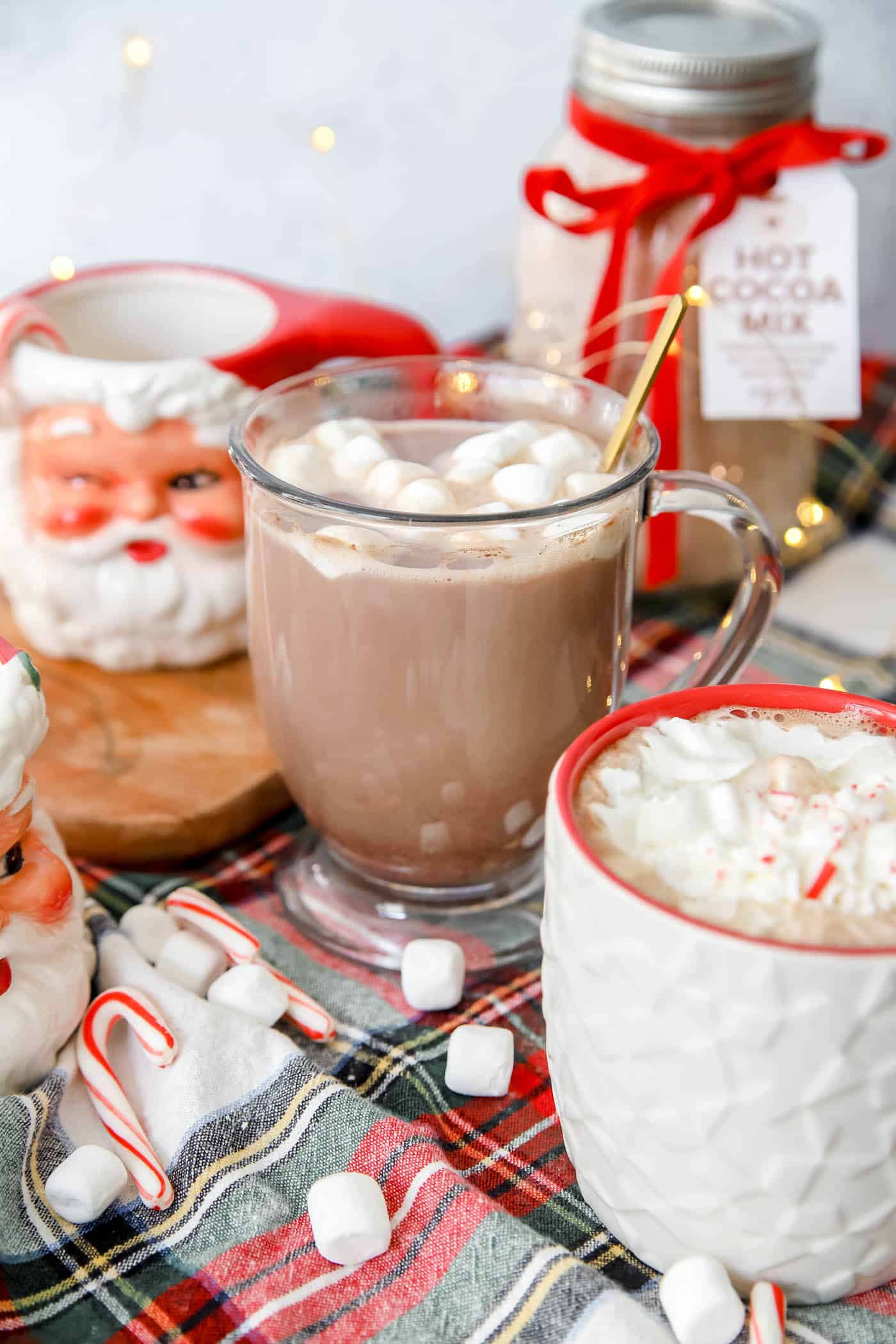 Hot chocolate in a mug with Santa mug and plaid table runner for Christmas.