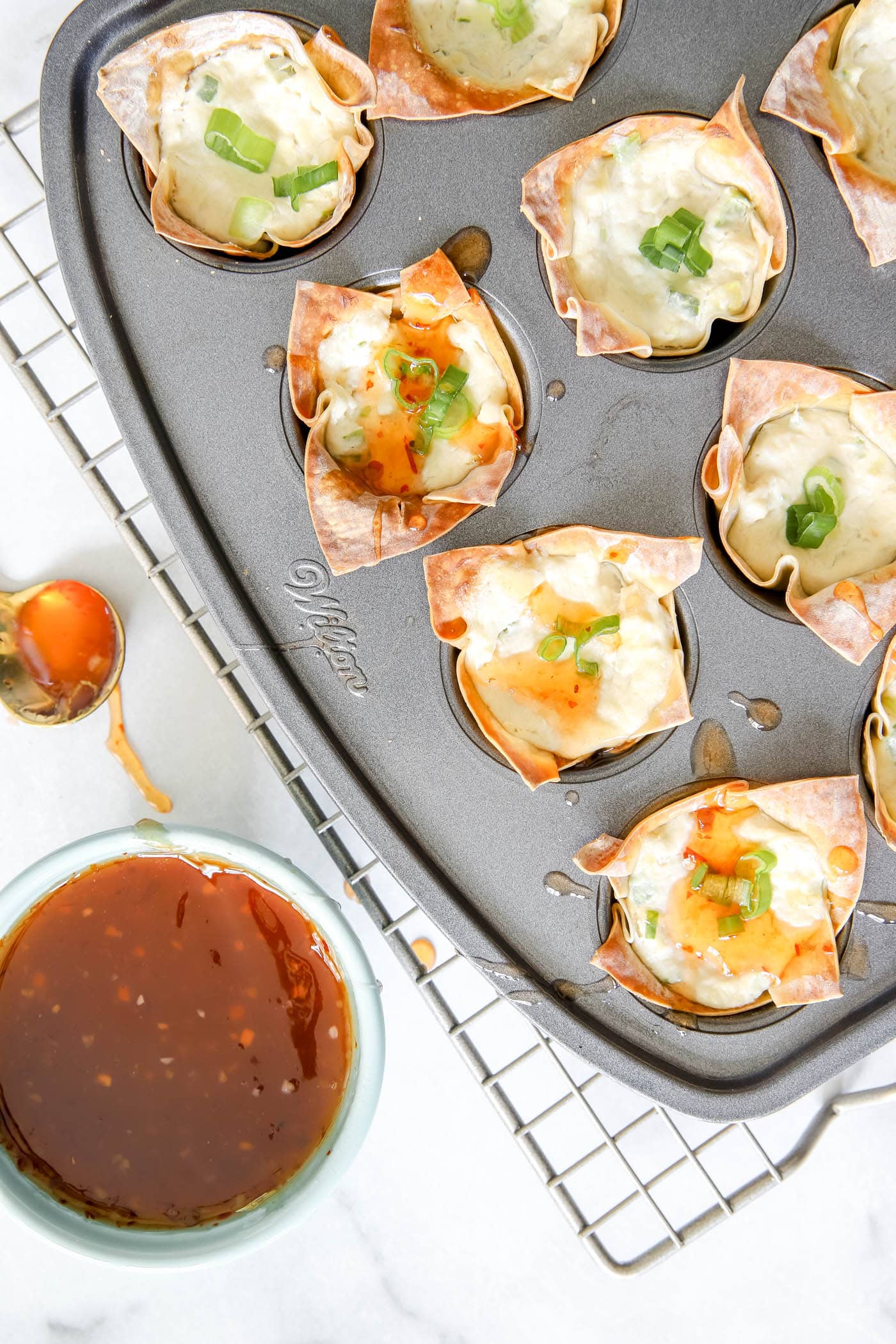 crab rangoon appetizers in a mini muffin pan with sweet and sour sauce.