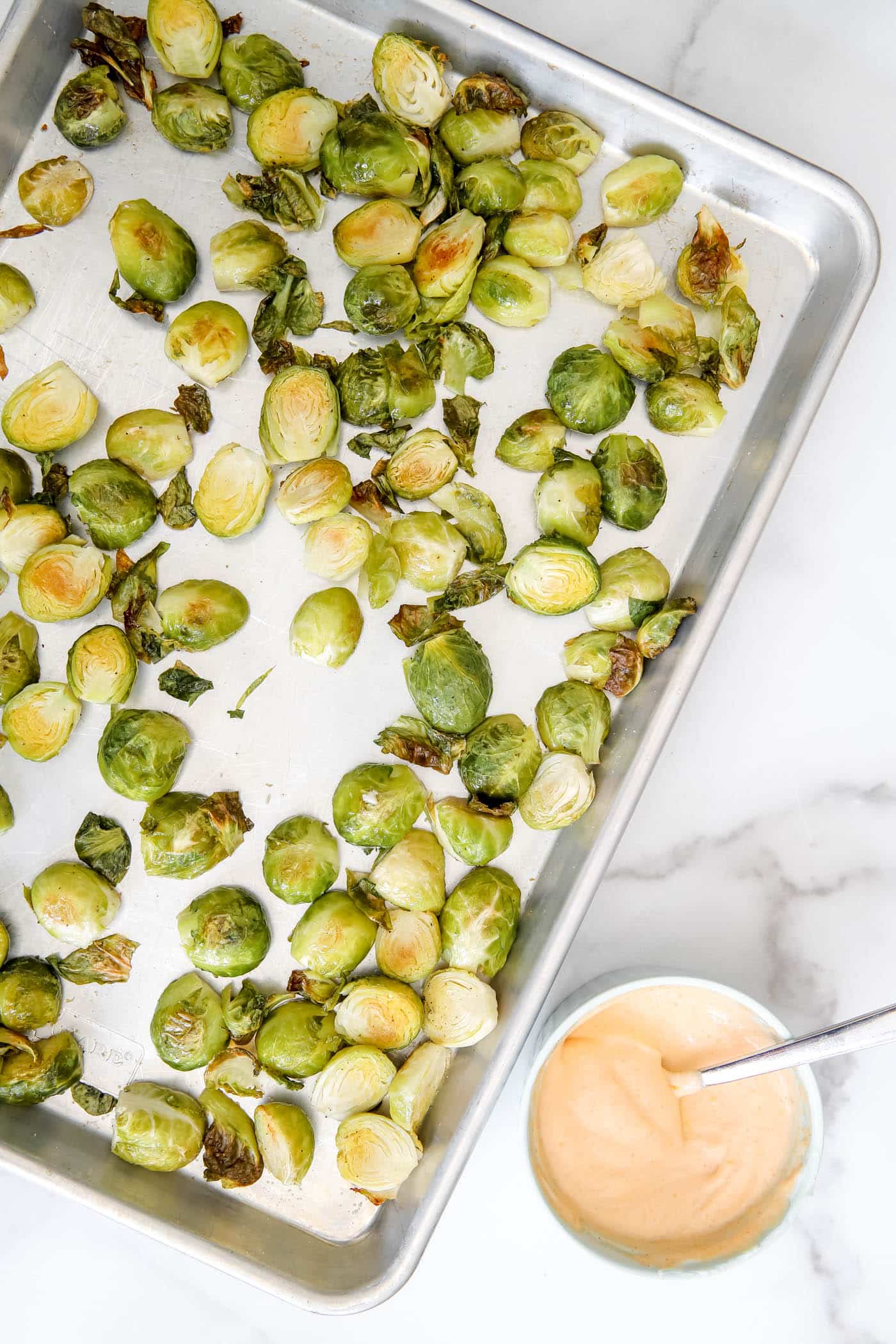 roasted Brussels sprouts on a sheet pan with sriracha mayo sauce.
