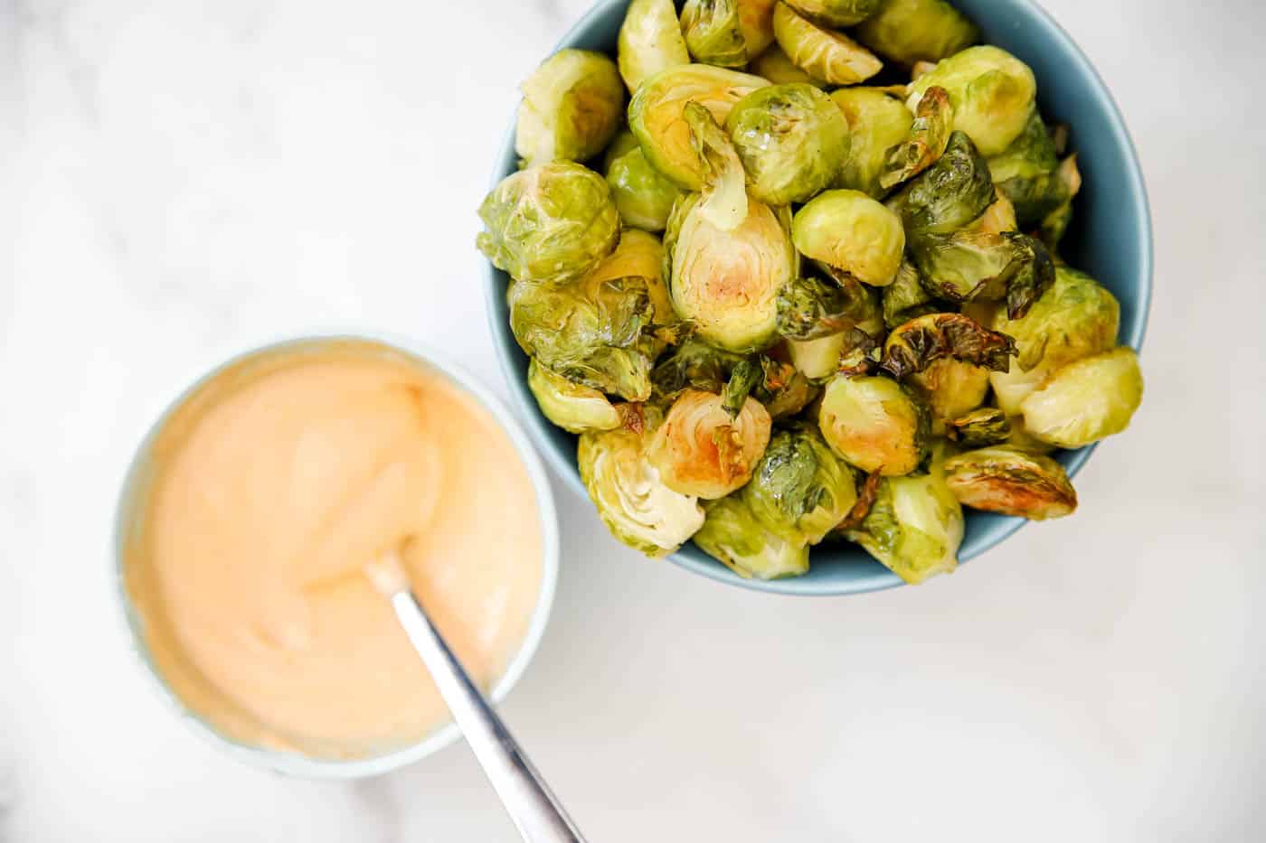 roasted Brussels sprouts on a sheet pan with sriracha mayo sauce.