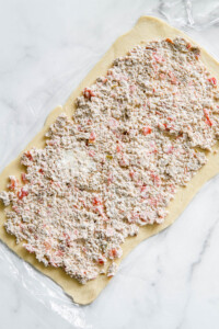 cover the crescent rolls with sausage and cheese mixture for Sausage and Cream Cheese Pinwheels recipe.