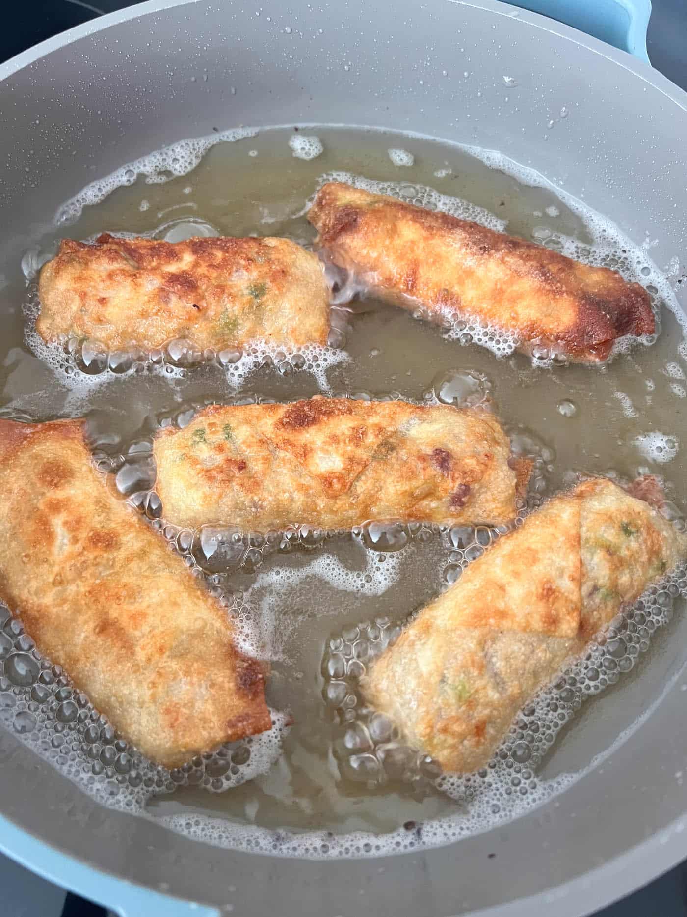 homemade egg rolls being fried in oil.